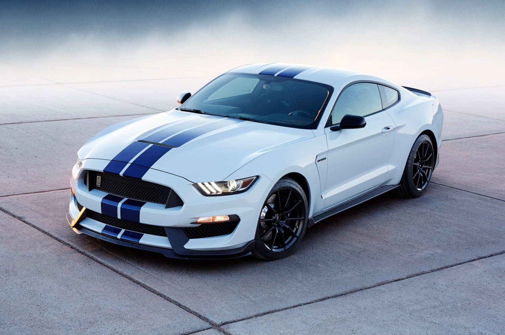White Ford Mustang Shelby GT350 muscle car with blue racing stripes parked on concrete, featured as an HD PC desktop wallpaper and background.