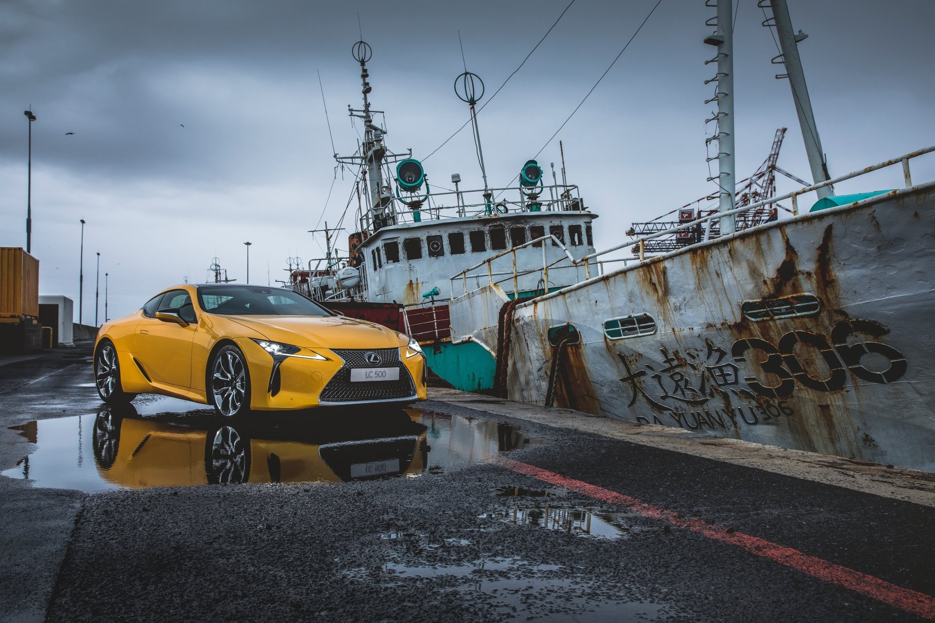 Yellow Lexus LC 500 grand tourer parked beside a weathered ship on a wet dock, captured in stunning 4K Ultra HD for a dynamic PC desktop background.