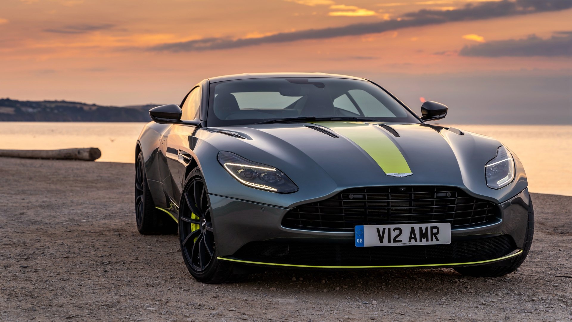 Silver Aston Martin DB11 supercar grand tourer parked by a scenic waterfront at sunset, captured in 4K Ultra HD as a PC desktop wallpaper and background.