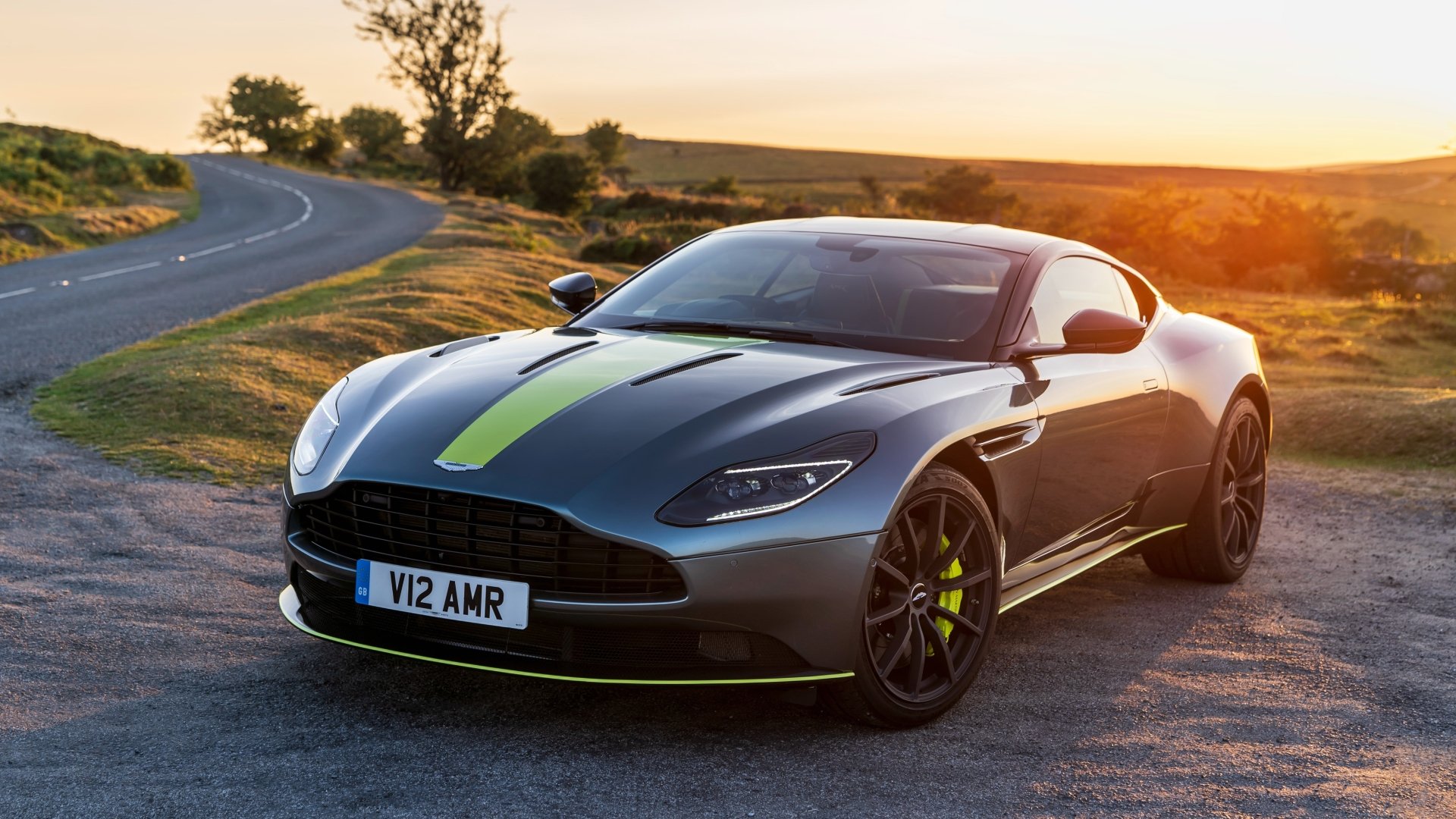Silver Aston Martin DB11 supercar with green stripe parked on a scenic road at sunset, showcased in 4K Ultra HD as a grand tourer vehicle wallpaper.