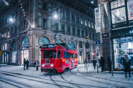 A red streetcar moves through a snowy winter street at night, surrounded by historic buildings and pedestrians, captured in HD for a desktop wallpaper.
