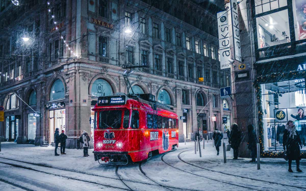 A red streetcar moves through a snowy winter street at night, surrounded by historic buildings and pedestrians, captured in HD for a desktop wallpaper.