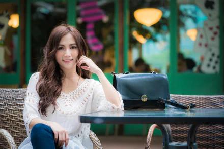 4K Ultra HD PC wallpaper: smiling brunette woman and model with long hair and brown eyes seated at a café table, bag on the table; soft depth-of-field background.