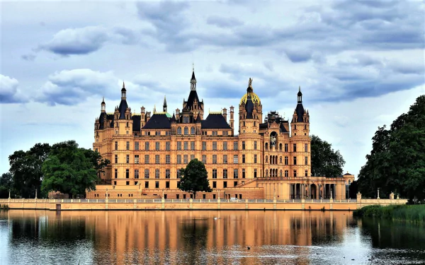 HD PC desktop wallpaper of Schwerin Palace — ornate man-made architecture reflected in a calm lake beneath a dramatic cloudy sky.