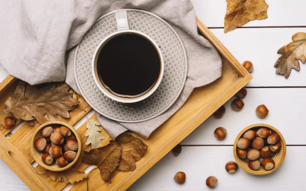 5K Ultra HD PC desktop wallpaper food still life: cup of black coffee on a tray with hazelnuts, bowls of hazelnuts and autumn leaves on white wood background.