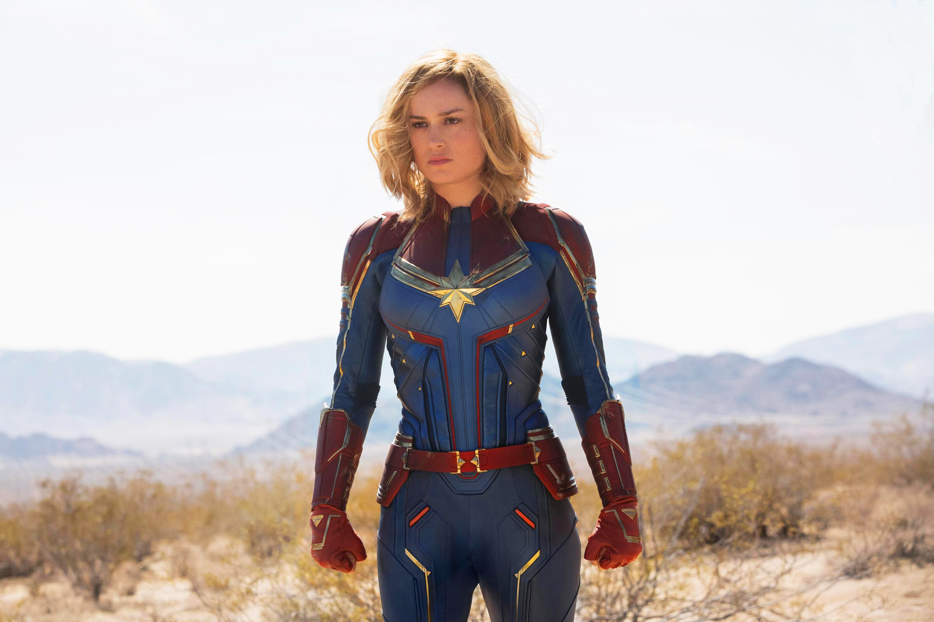 HD wallpaper featuring Brie Larson as Captain Marvel, standing in a desert with mountains in the background.