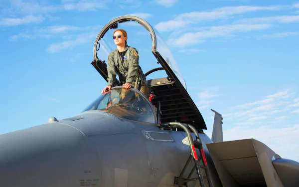 Brie Larson as Captain Marvel in a military jet cockpit against a blue sky, featured in a high-definition desktop wallpaper and background.