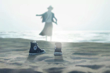 Anime-style HD desktop wallpaper featuring a pair of sneakers on sandy beach with a blurred figure walking toward the ocean in the background.