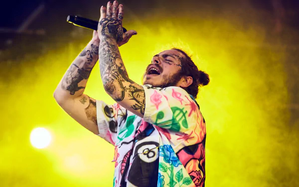 HD desktop wallpaper featuring Post Malone performing on stage with a microphone, showcasing his vibrant tattoos and colorful outfit.