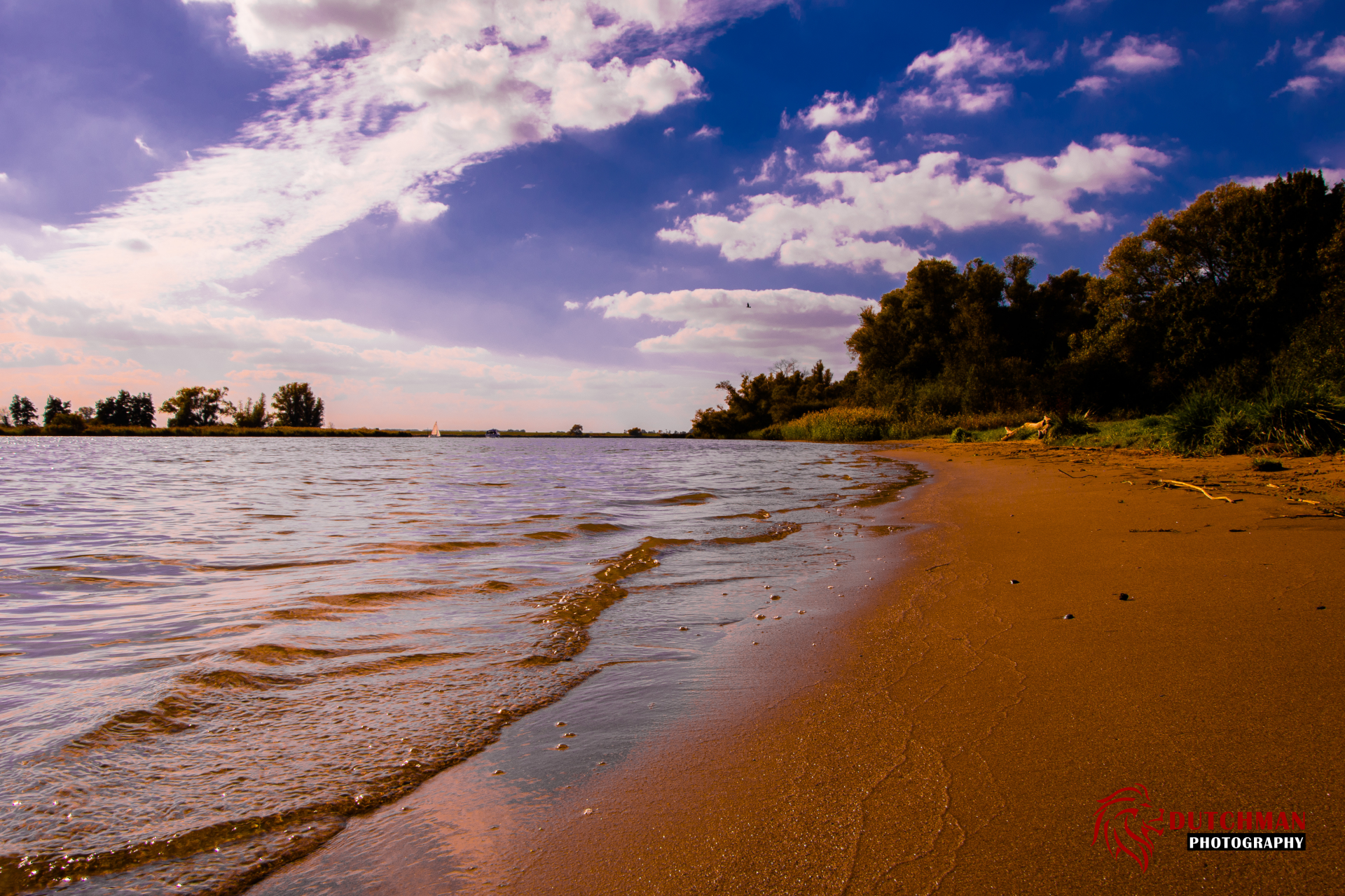 A 4K Ultra HD desktop wallpaper of a tranquil river meeting a sandy beach under a vibrant sky filled with clouds, framed by lush greenery along the shore.
