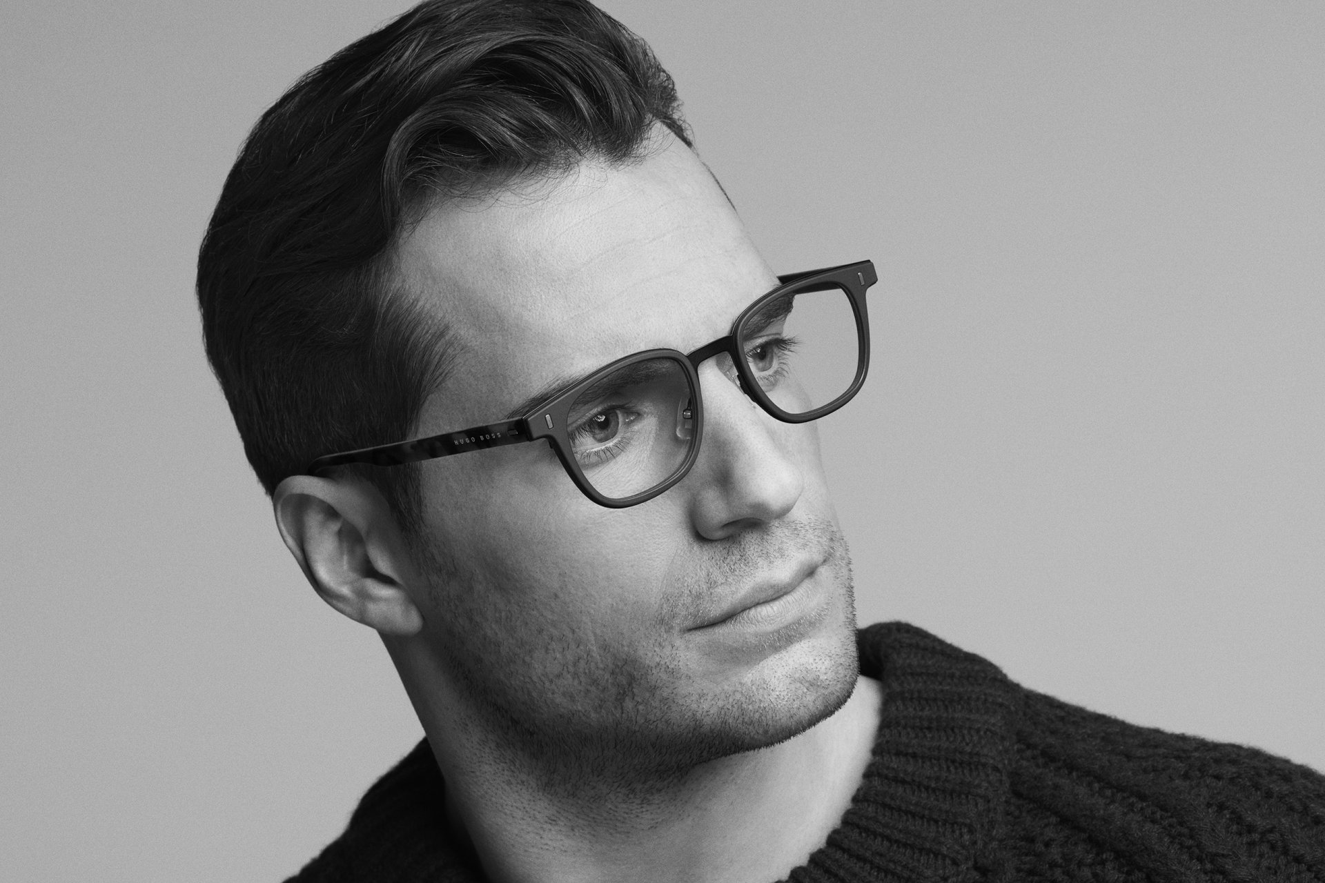 Black and white portrait of British actor Henry Cavill wearing glasses, captured in a thoughtful pose for an HD desktop wallpaper.