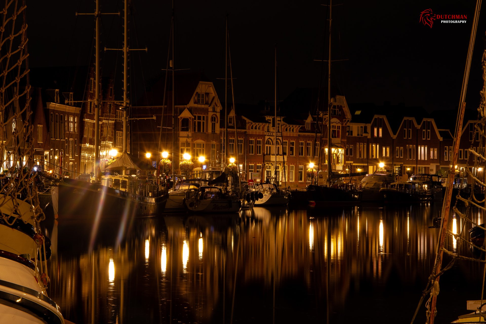 Night view of Hoorn harbor: man-made cityscape of historic buildings and moored ships reflecting warm lights on calm water — 5K Ultra HD PC desktop wallpaper