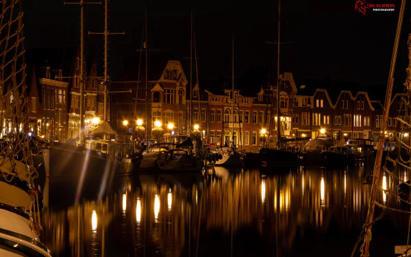 Night view of Hoorn harbor: man-made cityscape of historic buildings and moored ships reflecting warm lights on calm water — 5K Ultra HD PC desktop wallpaper