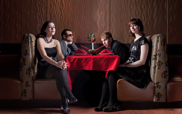 HD desktop wallpaper featuring members of Freezepop seated around a small table with a red tablecloth and a single rose, in a dimly lit room.