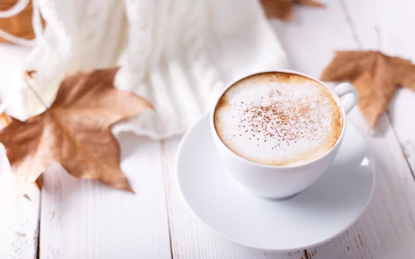 A cup of frothy coffee on a white saucer, surrounded by autumn leaves, captured in a 4K Ultra HD desktop wallpaper.