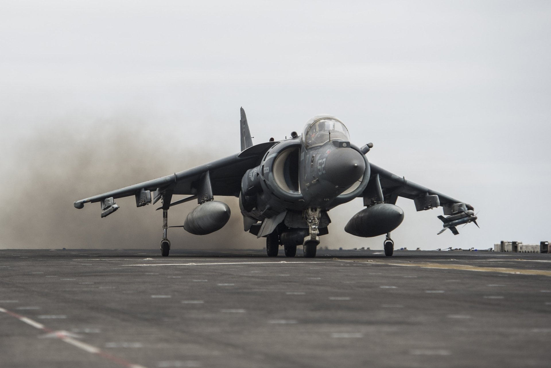 Front view of a McDonnell Douglas AV-8B Harrier II jet fighter on a carrier deck, exhaust plume kicking up — military warplane, 2K Quad HD PC desktop wallpaper background.