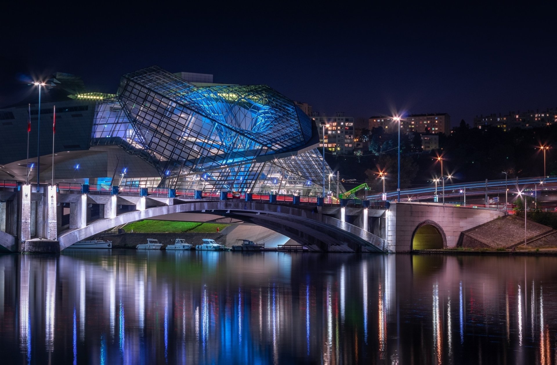 Night view of the illuminated Musée des Confluences in Lyon, France, showcasing its striking man-made architecture reflected on the water.