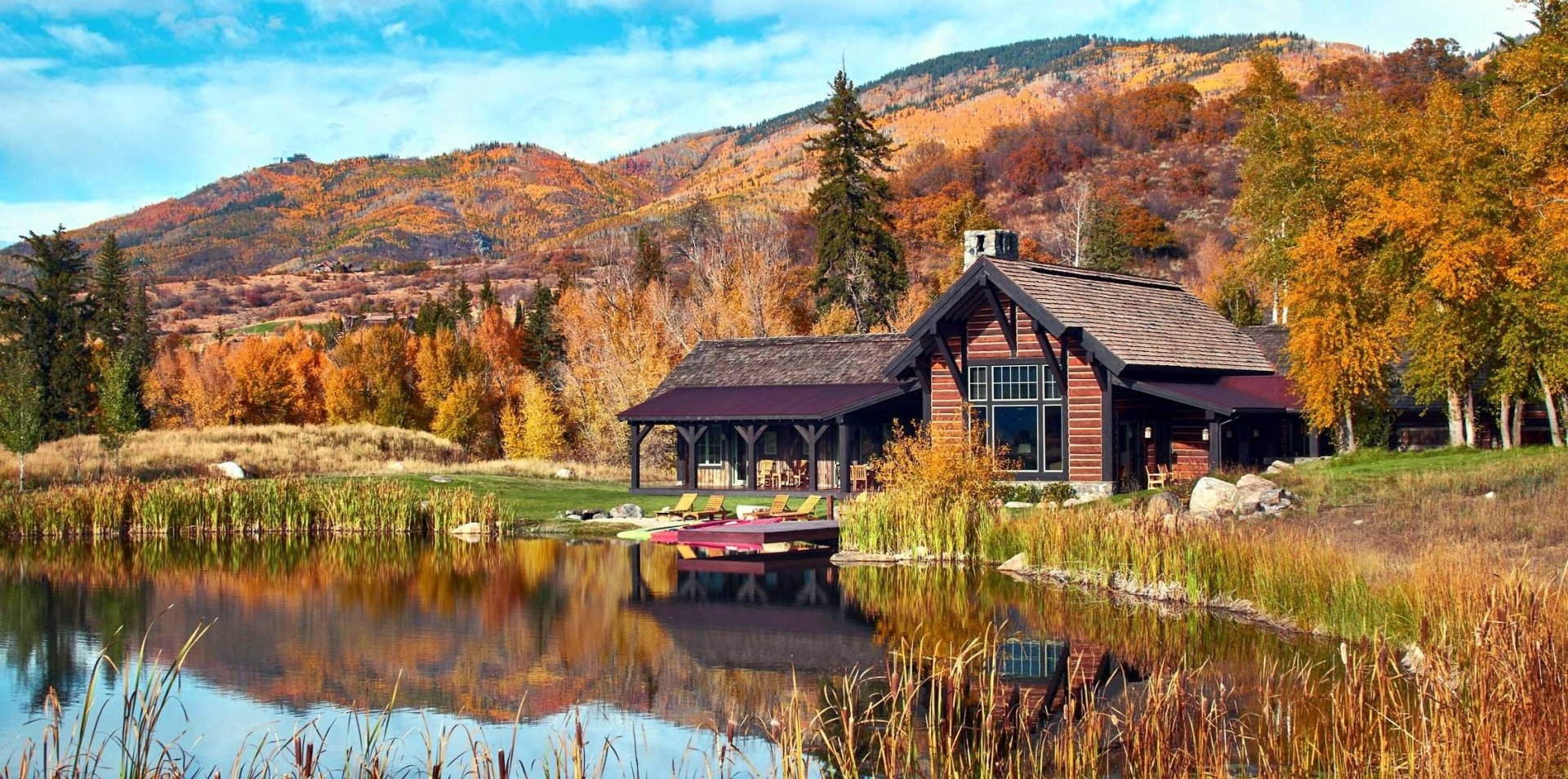 HD desktop wallpaper of a man-made house by a tranquil lake, surrounded by autumn-colored mountains and trees.