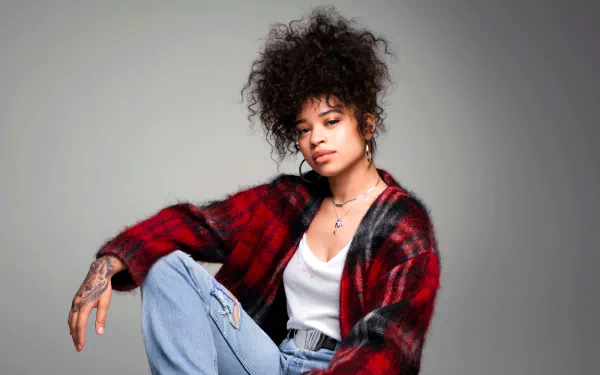 HD desktop wallpaper of Ella Mai seated in a casual pose, wearing a red flannel and jeans against a gray background.