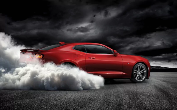 Red Chevrolet Camaro performing a smoky burnout on asphalt beneath dramatic storm clouds — 4K Ultra HD PC desktop wallpaper/background.