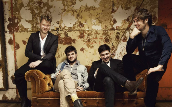 HD wallpaper of Mumford & Sons band members casually seated and leaning against a wall with peeling paint, exuding a relaxed and vintage vibe.