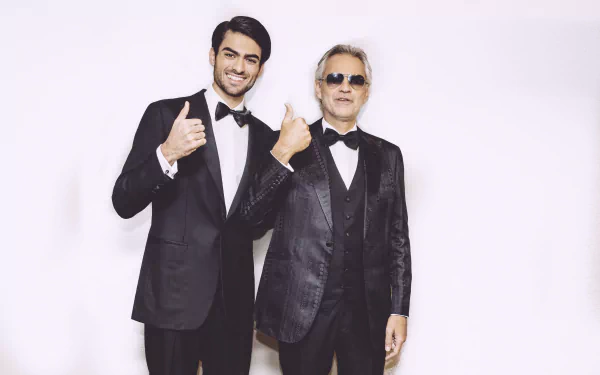 HD desktop wallpaper featuring Andrea Bocelli and another artist, both dressed in stylish tuxedos, smiling and giving a thumbs-up against a simple background.