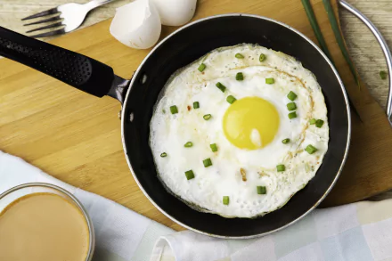 4K Ultra HD desktop wallpaper featuring a close-up of a fried egg garnished with chopped green onions in a black skillet on a wooden cutting board.