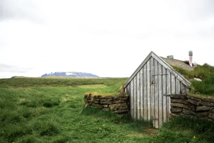 A rustic cabin with a turf roof stands in a grassy landscape in Iceland, captured in 4K Ultra HD as a serene PC desktop wallpaper.