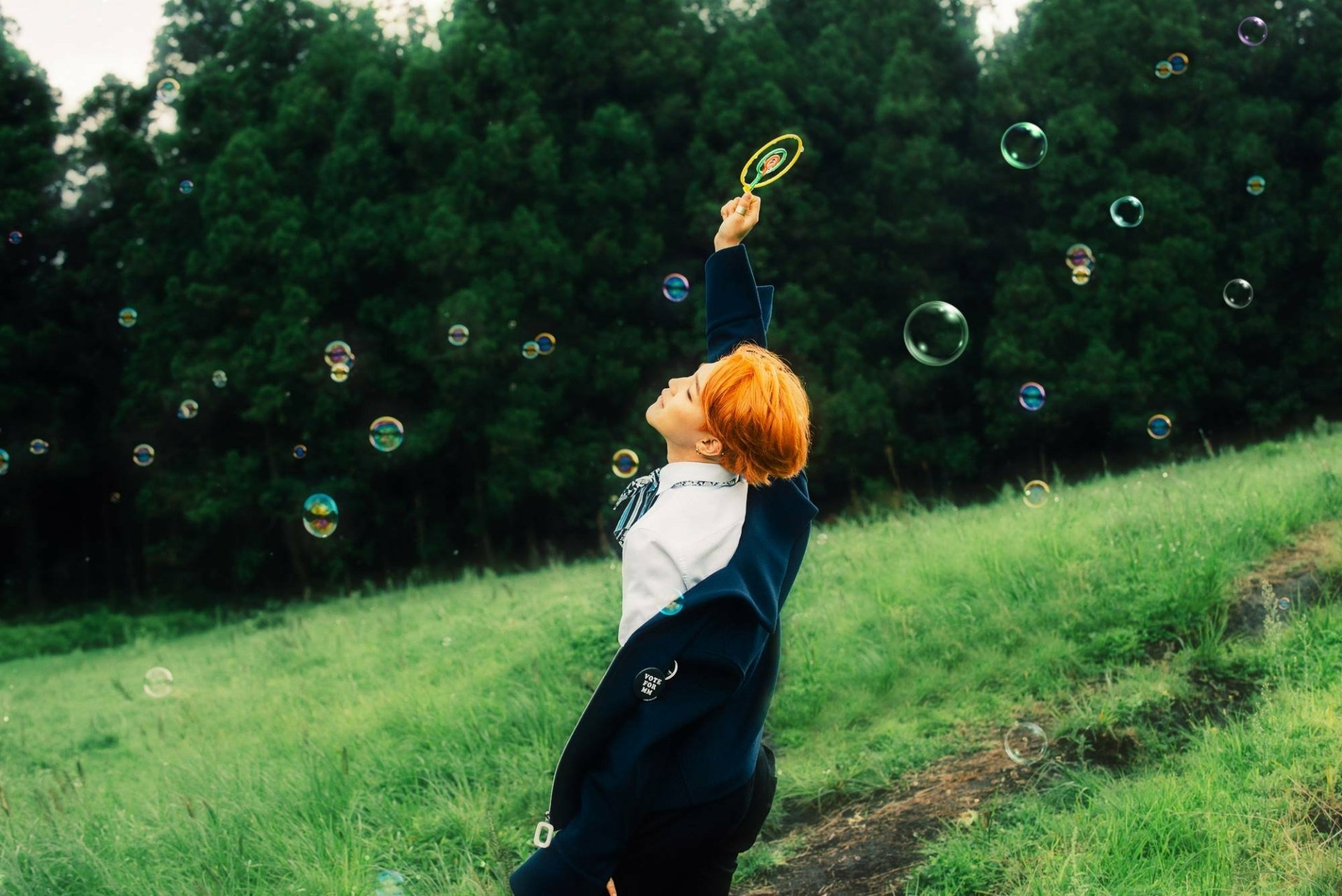 A vibrant HD wallpaper featuring Jimin from BTS, joyfully playing with bubbles in a grassy field, embodying the energetic spirit of K-pop music.