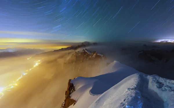 A breathtaking night scene capturing a snow-covered mountain under a star trail sky, with fog enveloping the horizon, showcasing the serene beauty of nature.