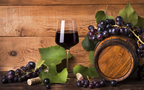 5K Ultra HD PC desktop wallpaper: rustic still-life of a wooden barrel, clusters of dark grapes, a glass of red wine and a cork on a wooden background.