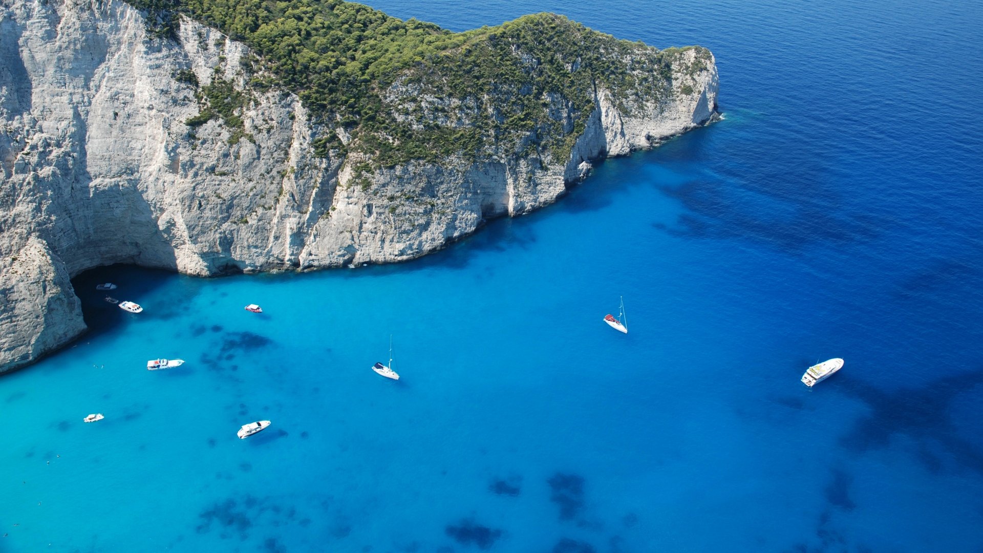 8K Ultra HD PC desktop wallpaper: aerial view of boats on vivid turquoise ocean waters beside towering white limestone cliffs.