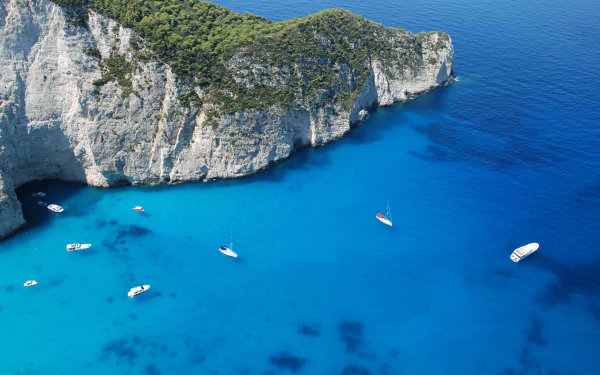 8K Ultra HD PC desktop wallpaper: aerial view of boats on vivid turquoise ocean waters beside towering white limestone cliffs.