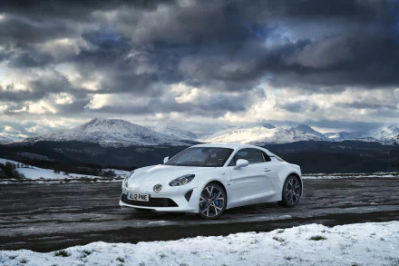 White Alpine A110 sports car parked on a snow-covered road with mountains and dramatic clouds — 2K Quad HD PC desktop wallpaper background.