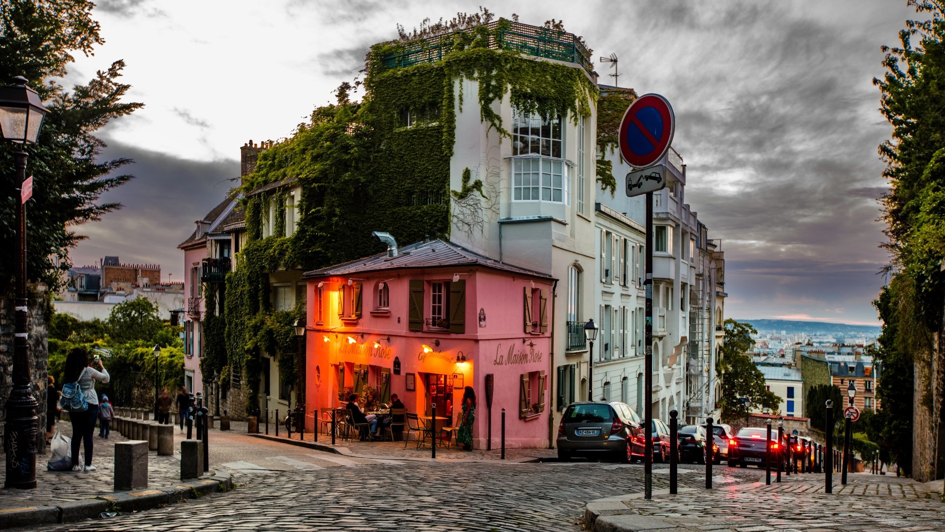 8K Ultra HD image of a charming Paris street corner with a cozy restaurant covered in greenery, set against a dramatic sky in the vibrant cityscape.
