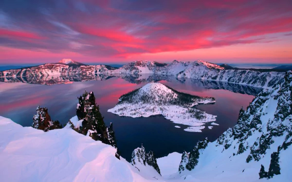 Snow-covered Crater Lake surrounded by snowy mountains under a vibrant pink winter sunset sky, showcasing stunning nature in this HD desktop wallpaper.