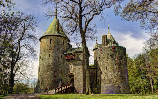 A medieval castle with stone towers surrounded by trees under a partly cloudy sky, captured in 4K Ultra HD quality for a PC desktop wallpaper.