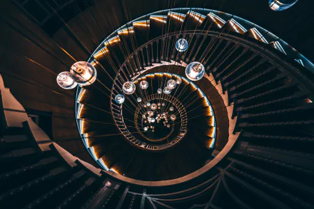 A 4K Ultra HD image of a man-made spiral staircase with illuminated steps and hanging lights, captured from above, creating a mesmerizing geometric pattern.