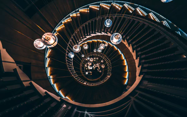 A 4K Ultra HD image of a man-made spiral staircase with illuminated steps and hanging lights, captured from above, creating a mesmerizing geometric pattern.