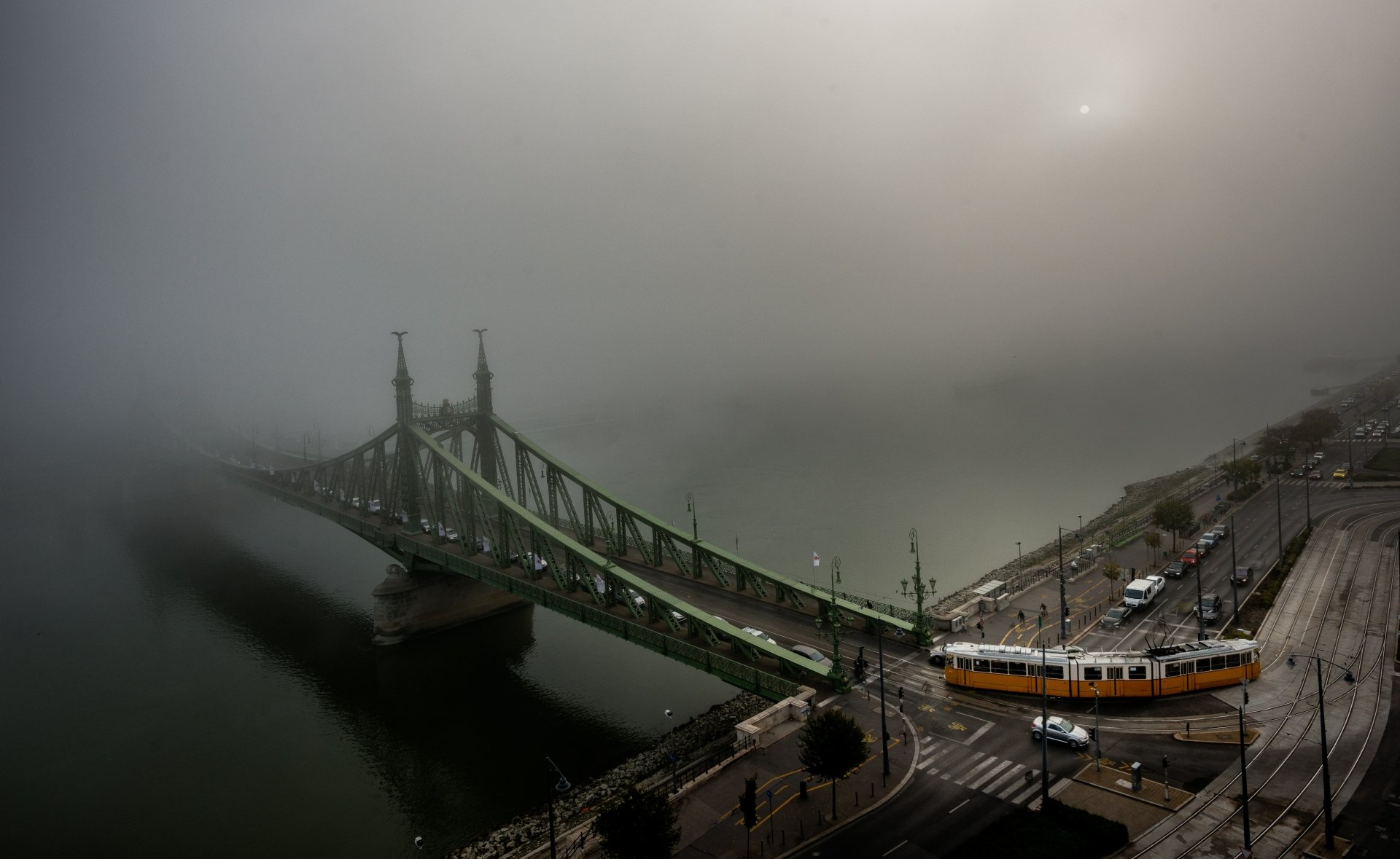 Foggy scene of a tram crossing a bridge over the Danube River in Budapest, Hungary, with roads and city structures visible in 4K Ultra HD detail.