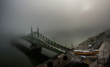 Foggy scene of a tram crossing a bridge over the Danube River in Budapest, Hungary, with roads and city structures visible in 4K Ultra HD detail.