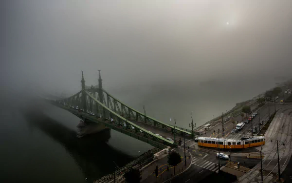Foggy scene of a tram crossing a bridge over the Danube River in Budapest, Hungary, with roads and city structures visible in 4K Ultra HD detail.